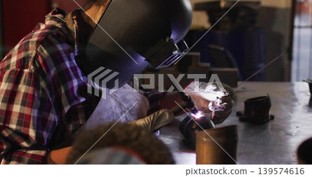 Welding welder using torch, feeding filler rod at metal shop bench, wearing helmet, apron, gloves Welding welder using torch, feeding filler rod at metal shop bench, wearing helmet, apron, gloves 139574616