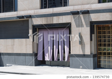 The entrance to a Japanese restaurant, with its purple noren (curtain) and stone exterior walls, creates a charming streetscape. 139574730