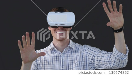 Smiling man wearing checked shirt in studio reaching interacting with white headset, dark wristband Smiling man wearing checked shirt in studio reaching interacting with white headset, dark wristband 139574862