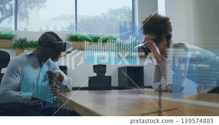 Wearing VR headsets two coworkers in shirt and sweater interacting at conference table, holograms Wearing VR headsets two coworkers in shirt and sweater interacting at conference table, holograms 139574885