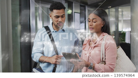 Standing colleagues in shirts examining tablet and carrying bags in office corridor, data overlay Standing colleagues in shirts examining tablet and carrying bags in office corridor, data overlay 139574964