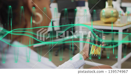 Holding woman with hoop earring scrolling smartphone in office, neon-green waveform overlay 139574967