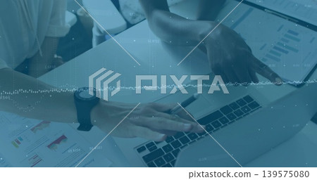 Pointing two women wearing business attire reviewing laptop charts at desk, printed pages and pen Pointing two women wearing business attire reviewing laptop charts at desk, printed pages and pen 139575080