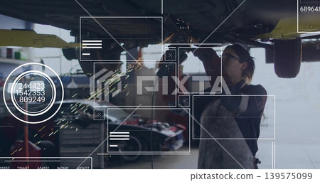 Grinding mechanic in apron and gloves using grinder under raised car in garage, producing sparks Grinding mechanic in apron and gloves using grinder under raised car in garage, producing sparks 139575099