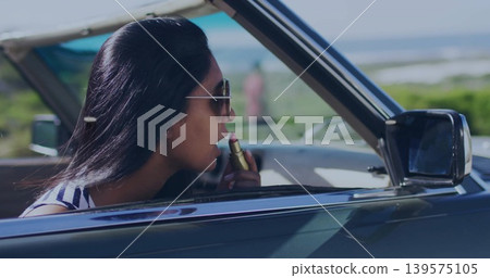 Applying lipstick Indian woman leaning out of droptop coast road with shades stripy top, copy space Applying lipstick Indian woman leaning out of droptop coast road with shades stripy top, copy space 139575105