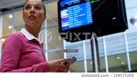 Checking woman in pink sweater holding phone scanning mounted info display at terminal, copy space Checking woman in pink sweater holding phone scanning mounted info display at terminal, copy space 139575208