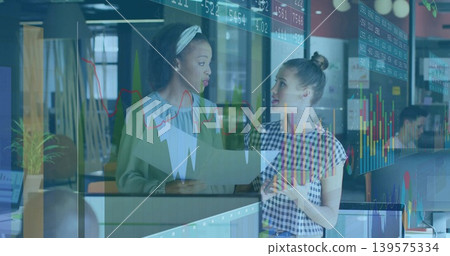 Discussing two women with headband comparing market charts on prints and tablet by glass partition Discussing two women with headband comparing market charts on prints and tablet by glass partition 139575334