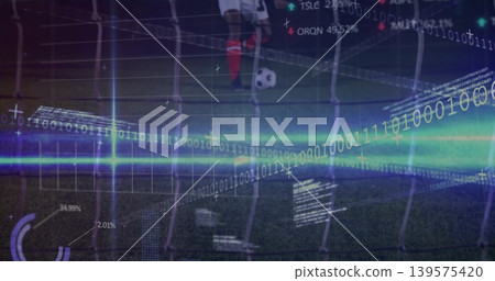 Standing soccer-player red-socked placing foot by ball on pitch at night, net and digital overlays Standing soccer-player red-socked placing foot by ball on pitch at night, net and digital overlays 139575420