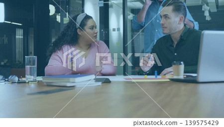 Gesturing woman in pink-sweater and man in dark-shirt discussing at glass room, blue marker visible 139575429