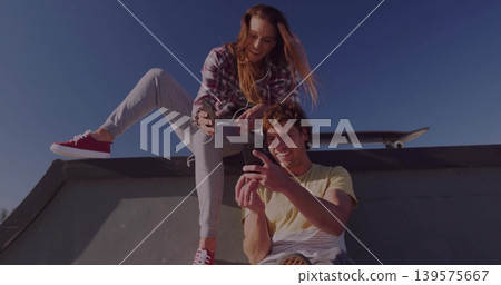 Perched couple scrolling phone at skate ramp, plaid, red sneakers, yellow tee, board, earbuds Perched couple scrolling phone at skate ramp, plaid, red sneakers, yellow tee, board, earbuds 139575667