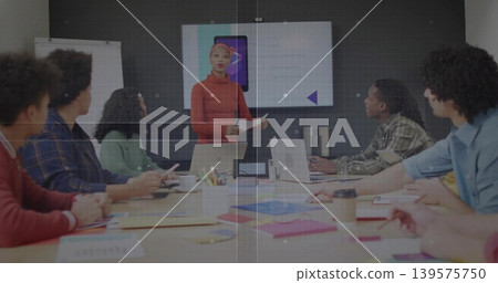 Presenting woman in red sweater and headwrap speaking in conference room, with screen and laptops 139575750