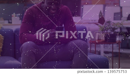 Sitting African American man wearing maroon shirt and watch, checking smartphone on sofa in lounge Sitting African American man wearing maroon shirt and watch, checking smartphone on sofa in lounge 139575753