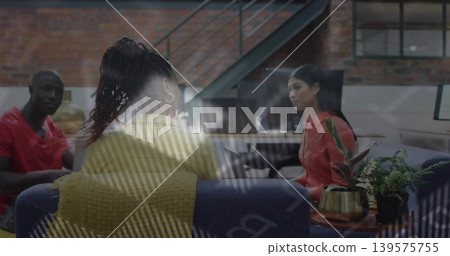 Discussing colleagues wearing yellow sweater and red tops on blue sofa in office, glass reflections Discussing colleagues wearing yellow sweater and red tops on blue sofa in office, glass reflections 139575755