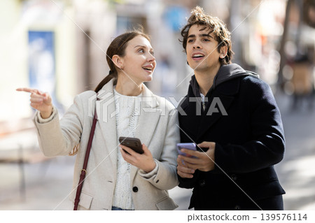 Young couple walking on street looking at phones for city map Young couple walking on street looking at phones for city map 139576114