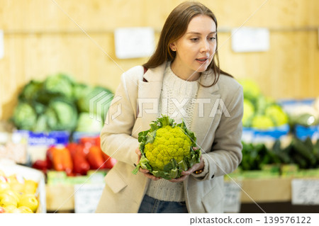 Girl near vegetable stand in store choose pick up broccoli cabbage Girl near vegetable stand in store choose pick up broccoli cabbage 139576122