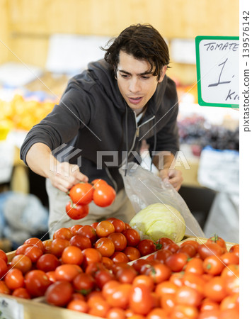 Man selects red tomatoes in the produce section of a supermarket. Names of vegetables in Spanish 139576142