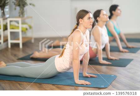 Young girl teaches yoga lesson, shows students technique of performing Urdhva Mukha Shvanasana asana Young girl teaches yoga lesson, shows students technique of performing Urdhva Mukha Shvanasana asana 139576318