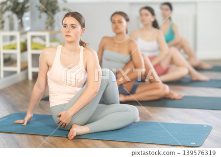 Young girl sitting in twisting asana Matsyendrasana at yoga class Young girl sitting in twisting asana Matsyendrasana at yoga class 139576319