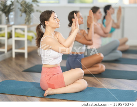 Young girl teaches yoga lesson, shows students technique of performing Gomukhasana asana 139576376