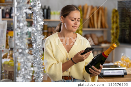 Young woman in store chooses bottle of sparkle wine, scan QR code on label 139576393