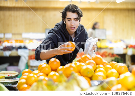 Young man chooses oranges in store Young man chooses oranges in store 139576408