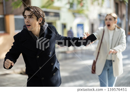 Male thief trying to snatch mobile phone of frightened woman on city Male thief trying to snatch mobile phone of frightened woman on city 139576451