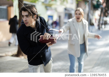 Young man snatching handbag from woman on street Young man snatching handbag from woman on street 139576455