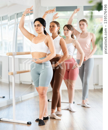 Group ballet rehearsal - young ballerinas stand in third position near ballet barre during group training in dance studio Group ballet rehearsal - young ballerinas stand in third position near ballet barre during group training in dance studio 139576496