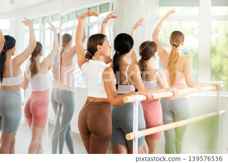 Group ballet rehearsal - young ballerinas stand in third position near ballet barre during group training in dance studio 139576536