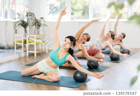 Young girl performing side bend with exercise ball in group pilates class 139576587