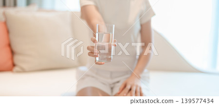 Healthy woman hold glass of clean mineral water glass on sofa at home, female drink pure water for hydration and wellness, fresh skin care, daily routine water intake, Refreshment and lifestyle Healthy woman hold glass of clean mineral water glass on sofa at home, female drink pure water for hydration and wellness, fresh skin care, daily routine water intake, Refreshment and lifestyle 139577434