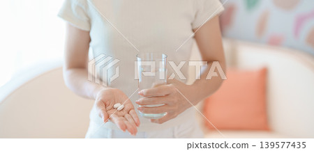 woman hand holding medicine painkiller pill and water glass on the sofa at home, taking for headaches, stomach ache, Diarrhea Pain from food poisoning, Endometriosis, Hysterectomy and Menstrual 139577435