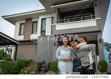 happy family, cheerful child girl piggy back on fatherwith mother while standing in front of their house 139577468