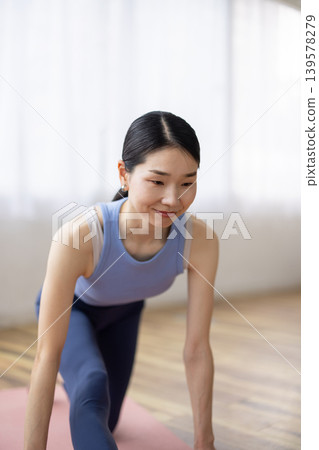 一位身穿瑜珈服的中年日本女性在明亮的窗邊紮起頭髮。 139578279