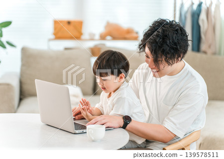 A parent and child spending time together in the living room while looking at a computer. A parent and child spending time together in the living room while looking at a computer. 139578511