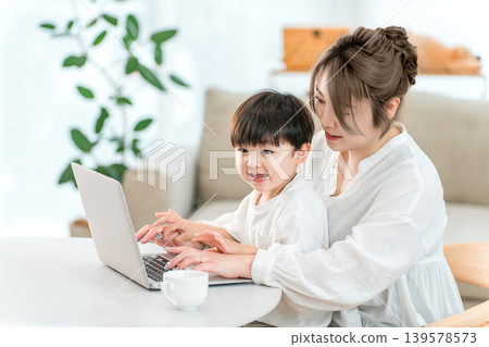 A parent and child spending time together in the living room while looking at a computer. A parent and child spending time together in the living room while looking at a computer. 139578573