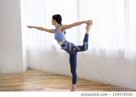 一位中年日本婦女在明亮的窗戶旁的墊子上擺出舞蹈姿勢。 139578585