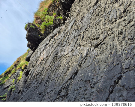 Steep rocky cliff with grass against blue sky Steep rocky cliff with grass against blue sky 139578616