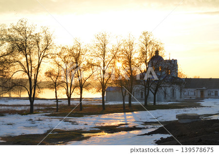 Sunset over snowy landscape with church and bare trees 139578675