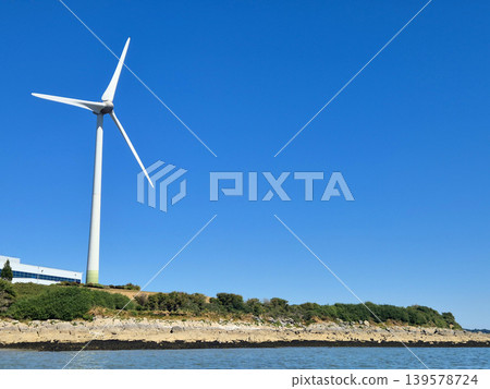 Wind Turbine by Coastal Shoreline Under Clear Blue Sky Wind Turbine by Coastal Shoreline Under Clear Blue Sky 139578724
