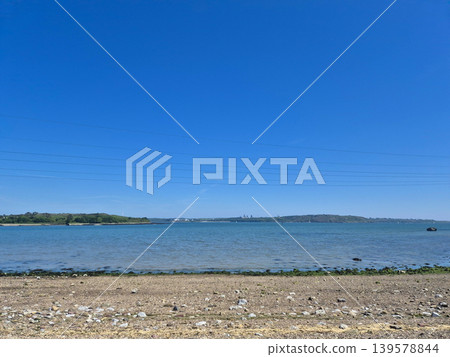 Rocky shoreline and calm sea under blue sky Rocky shoreline and calm sea under blue sky 139578844