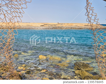 Rocky shoreline framed by rusted fishing net Rocky shoreline framed by rusted fishing net 139578845