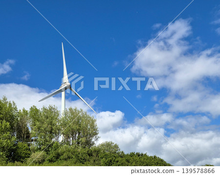 Wind turbine above trees under blue sky Wind turbine above trees under blue sky 139578866