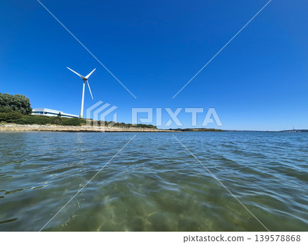 Wind turbine beside calm coastal water Wind turbine beside calm coastal water 139578868