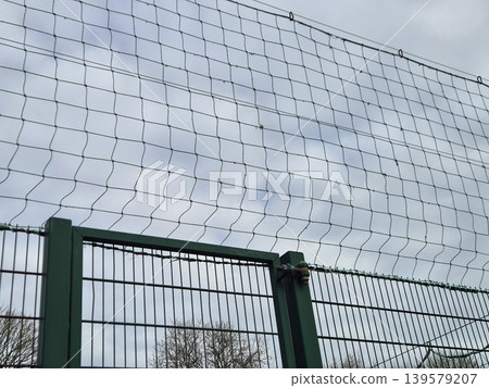 Metal fence with protective netting against cloudy sky Metal fence with protective netting against cloudy sky 139579207