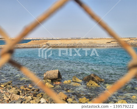 Coastal shoreline seen through blurred fence opening Coastal shoreline seen through blurred fence opening 139579222