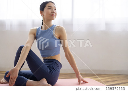 一位中年日本女性在明亮的窗邊，於瑜珈墊上練習雙魚座瑜珈姿勢。 139579333