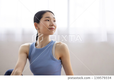 一位中年日本女性在明亮的窗邊，於瑜珈墊上練習雙魚座瑜珈姿勢。 139579334