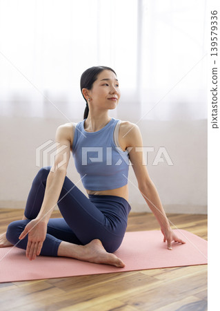 一位中年日本女性在明亮的窗邊，於瑜珈墊上練習雙魚座瑜珈姿勢。 139579336