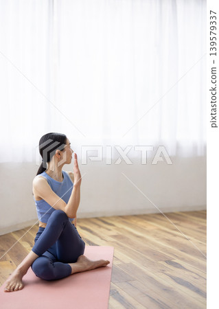 一位中年日本女性在明亮的窗邊，於瑜珈墊上練習雙魚座瑜珈姿勢。 139579337